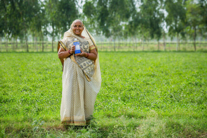 A person holding a bottle of soap in a field.